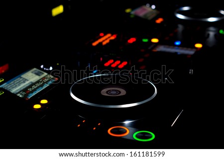 DJ turntable and music deck illuminated at night with colourful lights lighting up the knobs and controls for mixing audio soundtracks and recordings