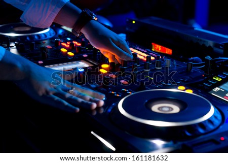 Hands of a DJ mixing music at a disco or concert with one hand on the switches and one held near the vinyl record on the turntable