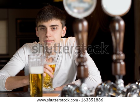 View between the beer taps on a dispenser of a serious young man drinking alone at the counter in the bar or pub