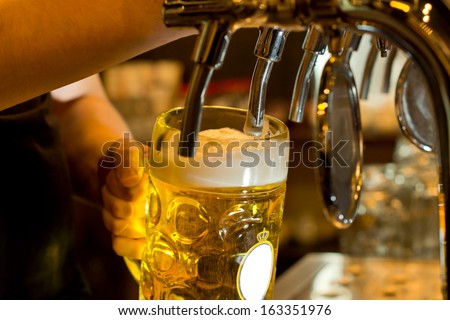 Close up of a male bartender dispensing draught beer in a pub holding a large glass tankard under a spigot attachment on a stainless steel keg