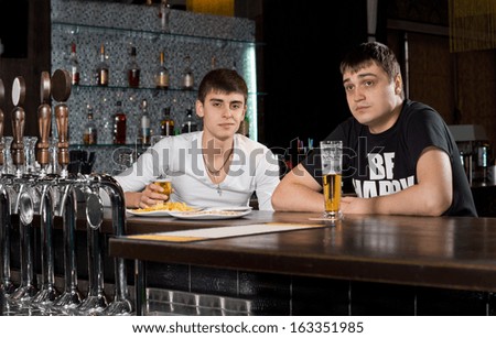 Two young teenage men drinking at the pub sitting at the counter in the bar enjoying a pint of beer