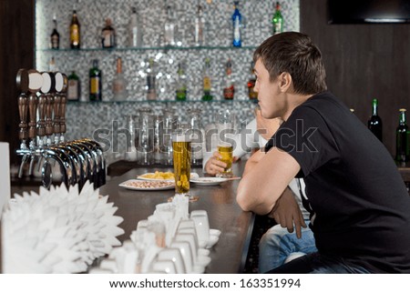 Two guys drinking beer together at a bar counter as they relax in the evening after work
