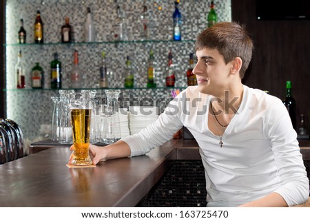 Young man enjoying a relaxing evening at the pub sitting at the bar counter with a chilled pint of draught beer
