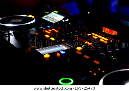 Closeup view at night of the colourful lights on the turntables and music mixing deck at a disco used by the DJ to mix and scratch audio for the dance or concert