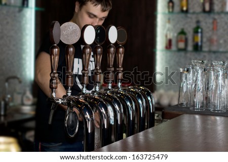 Young male bartender standing behind a counter in a pub or club dispensing draught beer