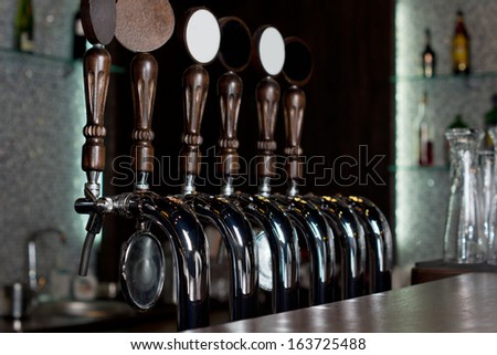 View across the counter of a row of beer taps on a stainless steel mechanical keg in a pub used to dispense draught beer
