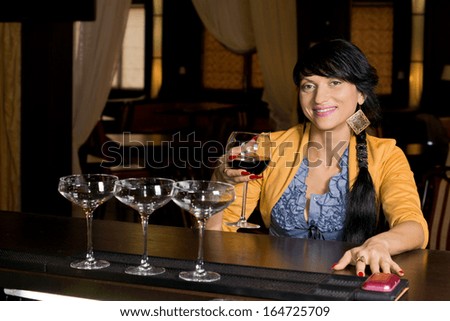 Smiling fashionable woman drinking at the bar raising her glass of red wine to the camera with a friendly smile