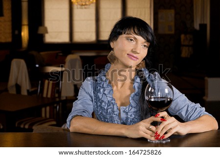 Lonely young woman drinking alone sitting at the bar counter with a large glass of red wine and a wistful dreamy expression