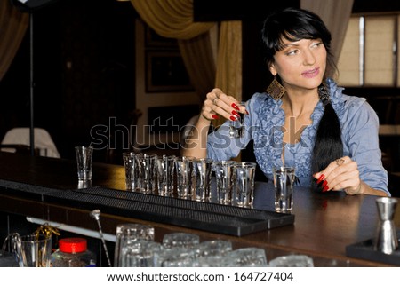 Attractive young woman drinking vodka shots at a bar sitting with a long line of shot glasses i front of her as she downs them followed by chasers