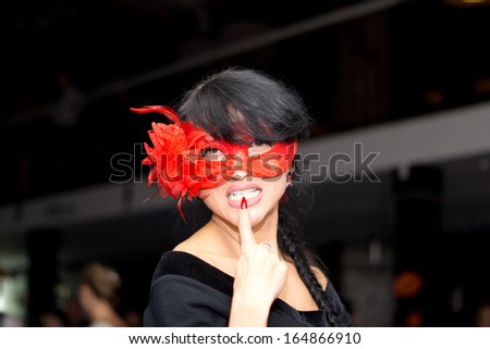 Nonconformist seductive mysterious brunette woman wearing a red Venetian masquerade eye mask, looking at camera provocatively
