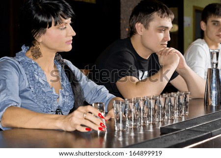 Woman drinking vodka at the bar with shot glasses lined up in a row in front of her staring thoughtfully at the line up