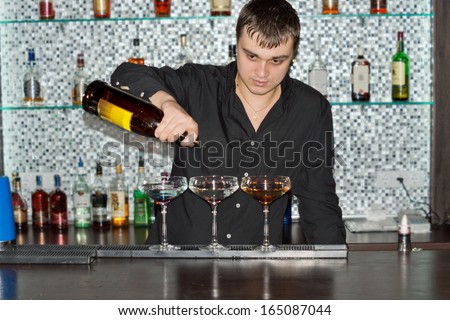 Barman pouring drinks at a bar into three elegant cocktail glasses as he prepares an exotic blend