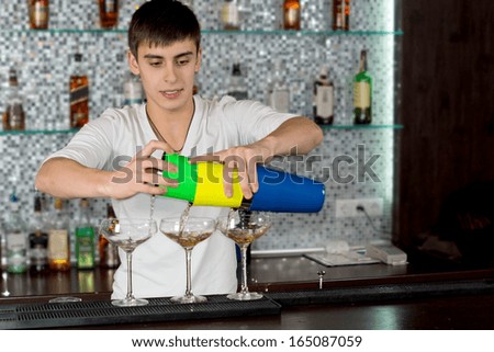 Bartender pouring a cocktail from a colourful cocktail shaker into three elegant glasses on the counter