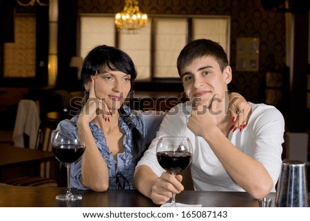 Happy young couple posing happy sitting at the bar drinking red wine in a fancy location
