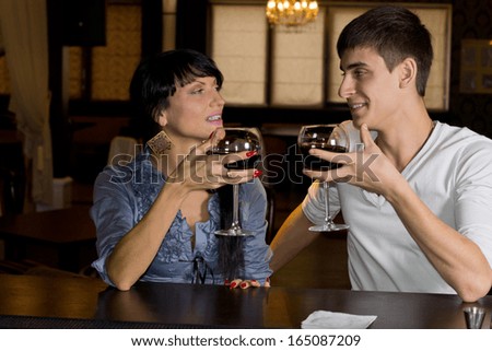 Young couple drinking red wine at a bar counter smiling and chatting as they look at each other and celebrate their friendship
