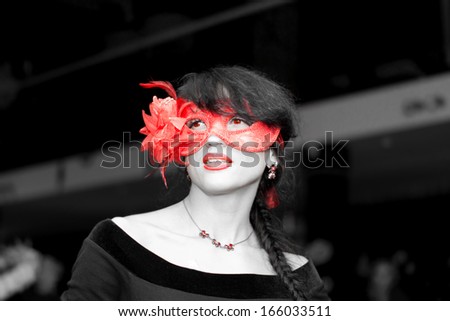 Nonconformist seductive young brunette woman wearing red lipstick and a red spectacular floral Venetian masquerade eye mask in a crowded hall