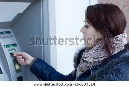 Woman using an Automated Teller machine at a bank inserting her bankcard into the slot of the machine to start her withdrawal transaction