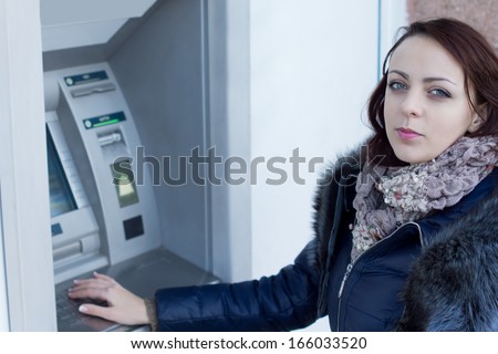 Young woman standing at an ATM machine outside a bank waiting to withdraw money from automated teller