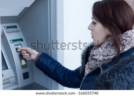 Woman retrieving her bank card at the ATM waiting for it to be dispensed from the slot after she has made a cash withdrawal