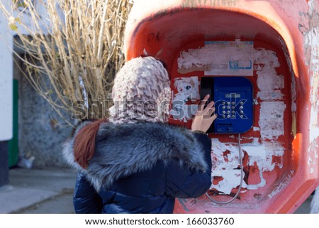 Person in a headscarf standing with their back to the camera talking on a public pay phone as she connects to an emergency number or friend