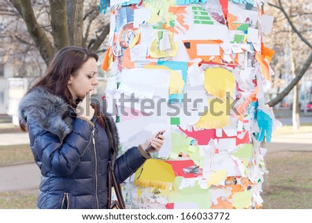 Woman reading a notice that she has taken off a public noticeboard in a town park as she contemplates contacting the advertiser