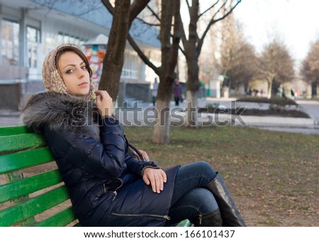 Woman wrapped up warmly against the chilly winter weather sitting relaxing or waiting for someone on a bench in an urban park