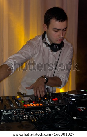 Handsome young disc jockey mixing music at a deck concentrating while scratching the vinyl records on the turntables and controls the switches at a nightclub