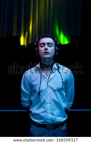 Man standing enjoying the music on his earphones as he relaxes in the darkness with his head tilted back and eyes closed as he concentrates on the soundtrack