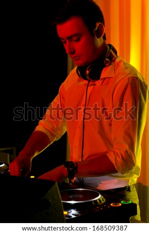 Disc jockey working at his deck and turntables mixing music in colourful party lighting with a warm orange glow