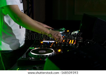 Close up of the hands of a young male disc jockey mixing and blending music tracks on his deck in the darkness of a party or nightclub