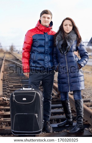 Young couple going off on vacation standing arm in arm with their suitcase in the centre of the train track on the wooden sleepers waiting for the train