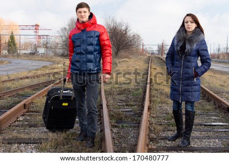 Young couple waiting on the railway tracks with a packed suitcase for the arrival of the train and the start of their annual vacation
