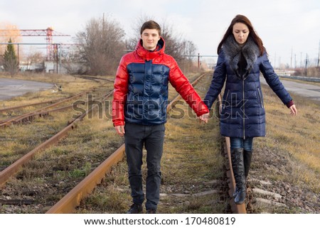 Couple taking a quiet stroll along the railway lines holding hands as the young woman balances on the metal track
