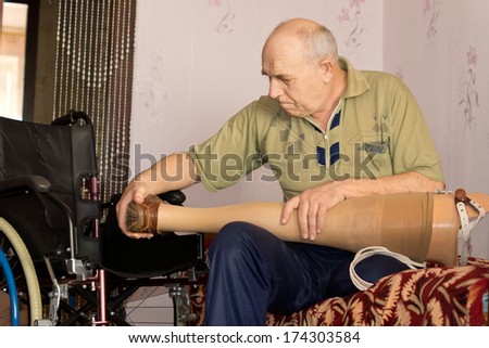 Senior man sitting on his bed checking out his artificial leg before fitting it to his stump following an amputation