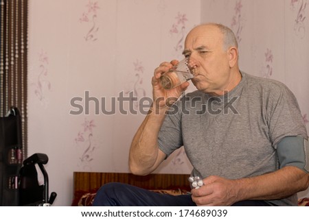 Elderly man taking his medication drinking the tablets down with a glass of water