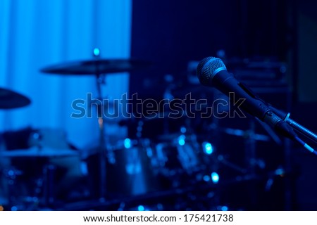 Microphone in front of the bands instruments standing ready on a stage for a live performace at a rock or jazz concert or festival in colourful blue lighting