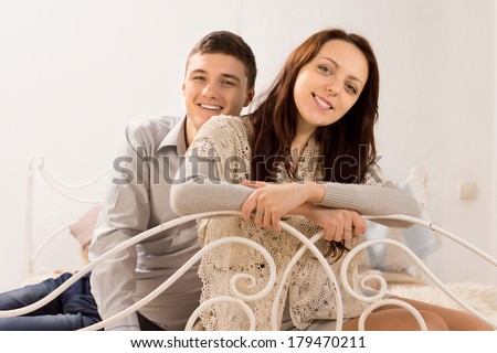 Smiling beautiful happy couple in stylish clothes on a wrought iron bed leaning over the white curving rail looking at the camera with charming friendly smiles