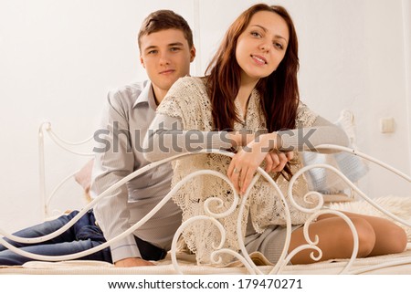 Attractive friendly stylish young couple relaxing on an old vintage wrought iron bed with curved a white rail smiling at the camera