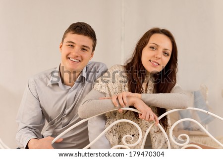 Happy laughing stylish young couple relaxing together at home sitting on a wrought iron sofa or bed leaning over the rail looking at the camera