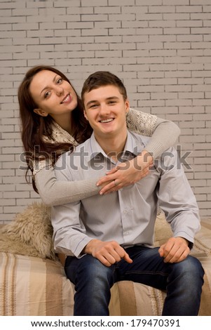 Charming smiling couple in an affectionate embrace sitting on a sofa in front of a painted interior brick wall