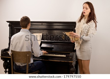 Young couple giving a classical duet with an attractive stylish young woman singing from a music score accompanied by a young man on a piano