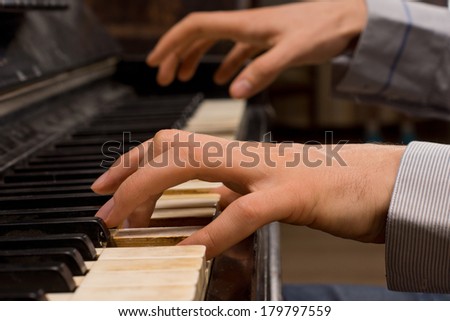 Close up of the hands of a male pianist playing music on an ivory keyboard on an old piano as he practices for a performance