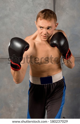 Handsome muscular young boxer standing with his gloved fists raised and a look of determined concentration on his face