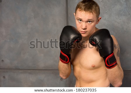 Young boxer with a mean look standing with his gloved fists raised to his chest staring at the camera against a metal background with copyspace