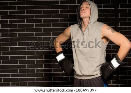 Young boxer doing breathing exercises before a fight standing with his gloved hands on his hips and head tilted back in the darkness with copyspace