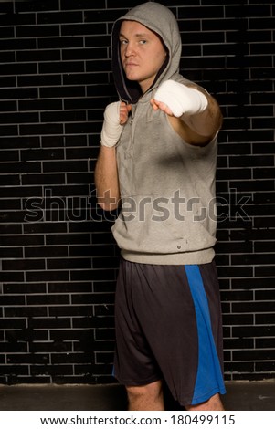 Serious young boxer standing punching his bandaged fist at the camera as he trains for his next match in front of a dark brick wall