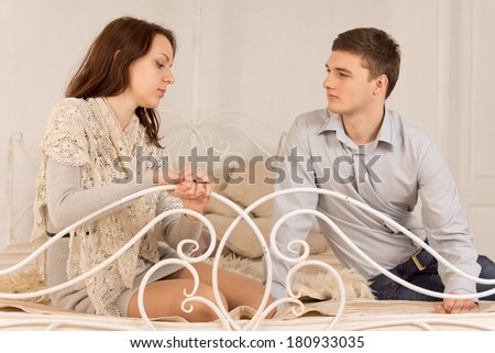 Stylish young couple sitting on a wrought iron bed with on ornate rail having a serious discussion