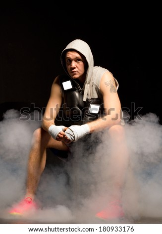 Young boxer planning his strategy sitting on a stool with smoke billowing around his feet concentrating deeply with a contemplative expression