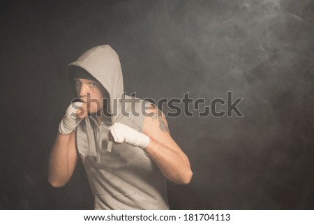 Muscular boxer ready for a fight standing with his fists raised looking out intently from under his hooded top as he watches his opponent carefully against a dark background with copyspace