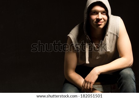 Shadowy portrait of a smiling young man in a hoodie crouching down in the darkness, with copyspace
